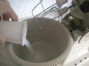 The sugar being poured from a cup into the mixing bowl