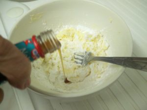 Butter, icing sugar mixed in a bowl, with vanilla essence being poured in