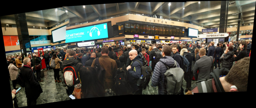 A panoramic shot showing the crowds and display boards at London Euston station